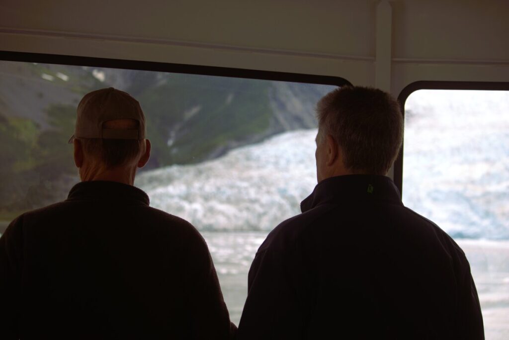Joe and Keith silhouetted against a glacier viewed through a boat window in Alaska