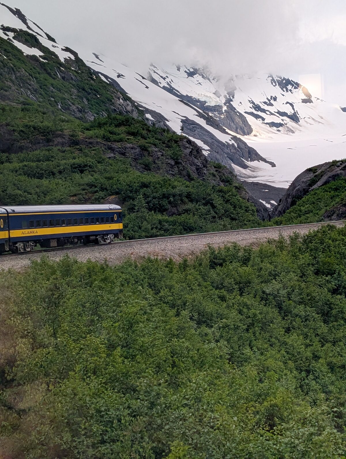 Alaska Railroad train winding through mountain scenery with a glacier in the background