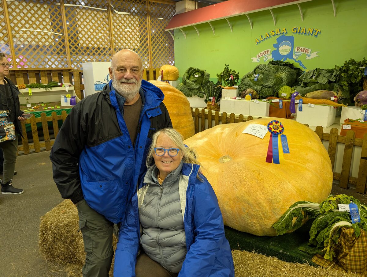 Mike and Phyllis posing next to a 1,820 lb prize-winning giant pumpkin at the Alaska Giant vegetable display, Alaska State Fair